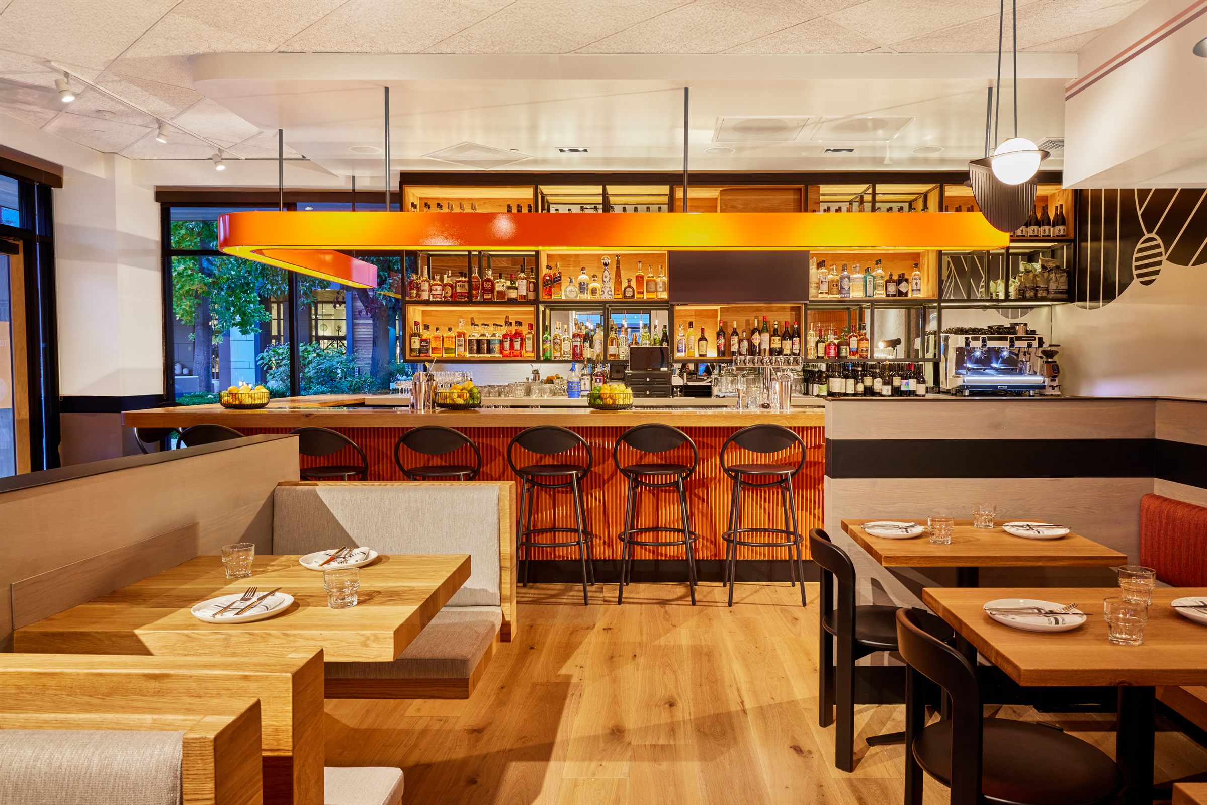 Bright restaurant bar with orange lighting, wood tables, and backlit spirits display