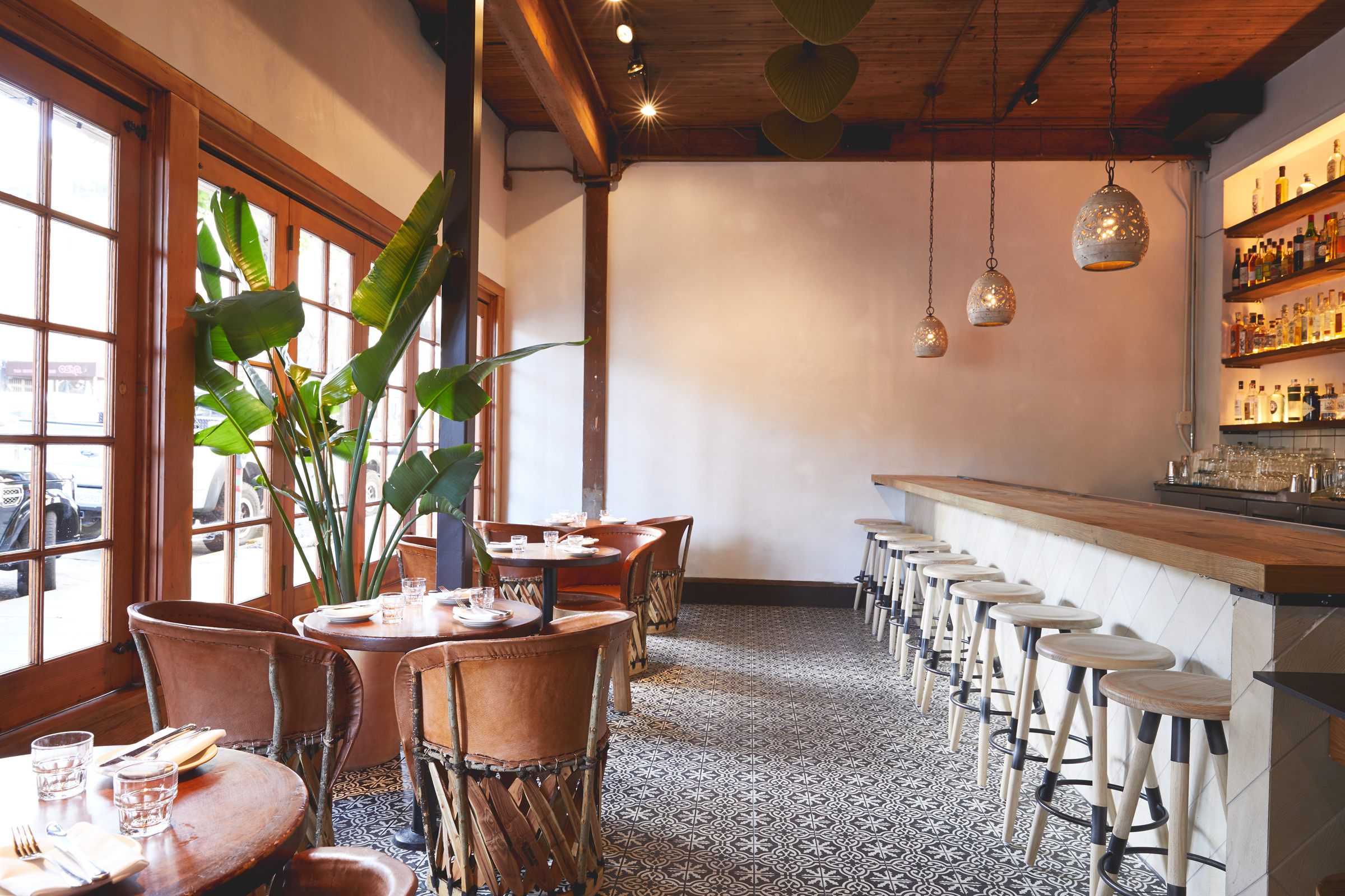 Warm restaurant dining room with wood windows, bar seating, and tropical plants